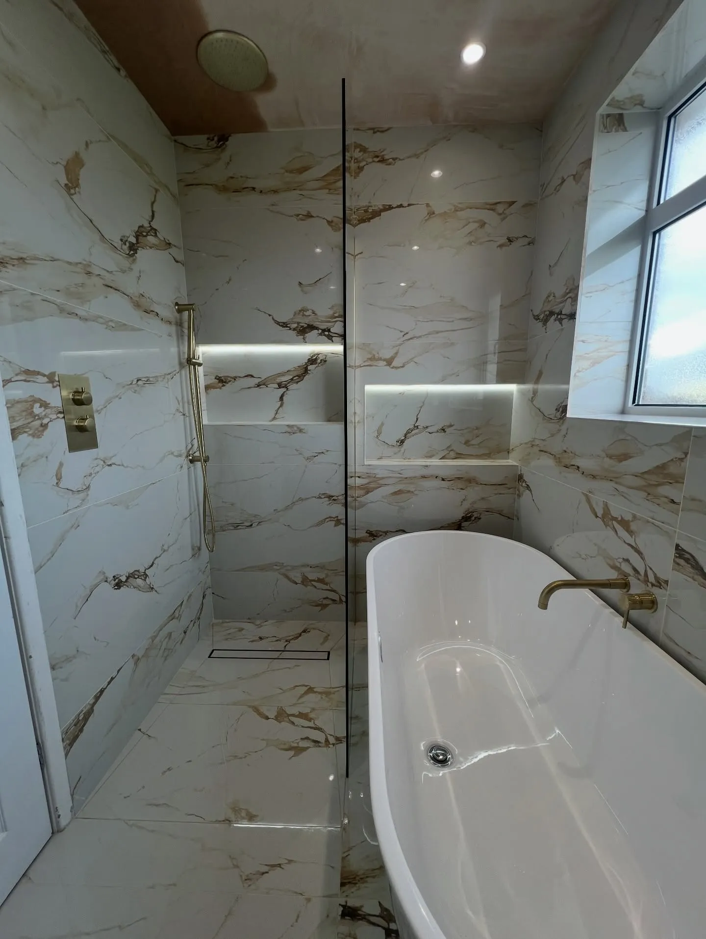 The finished bathroom — calacatta gold porcelain, freestanding bath and brushed brass fittings