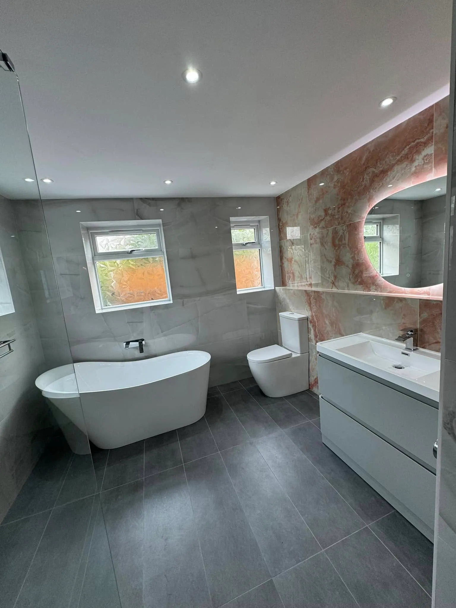 Full view of the onyx bathroom: freestanding bath, vanity and backlit pebble mirror