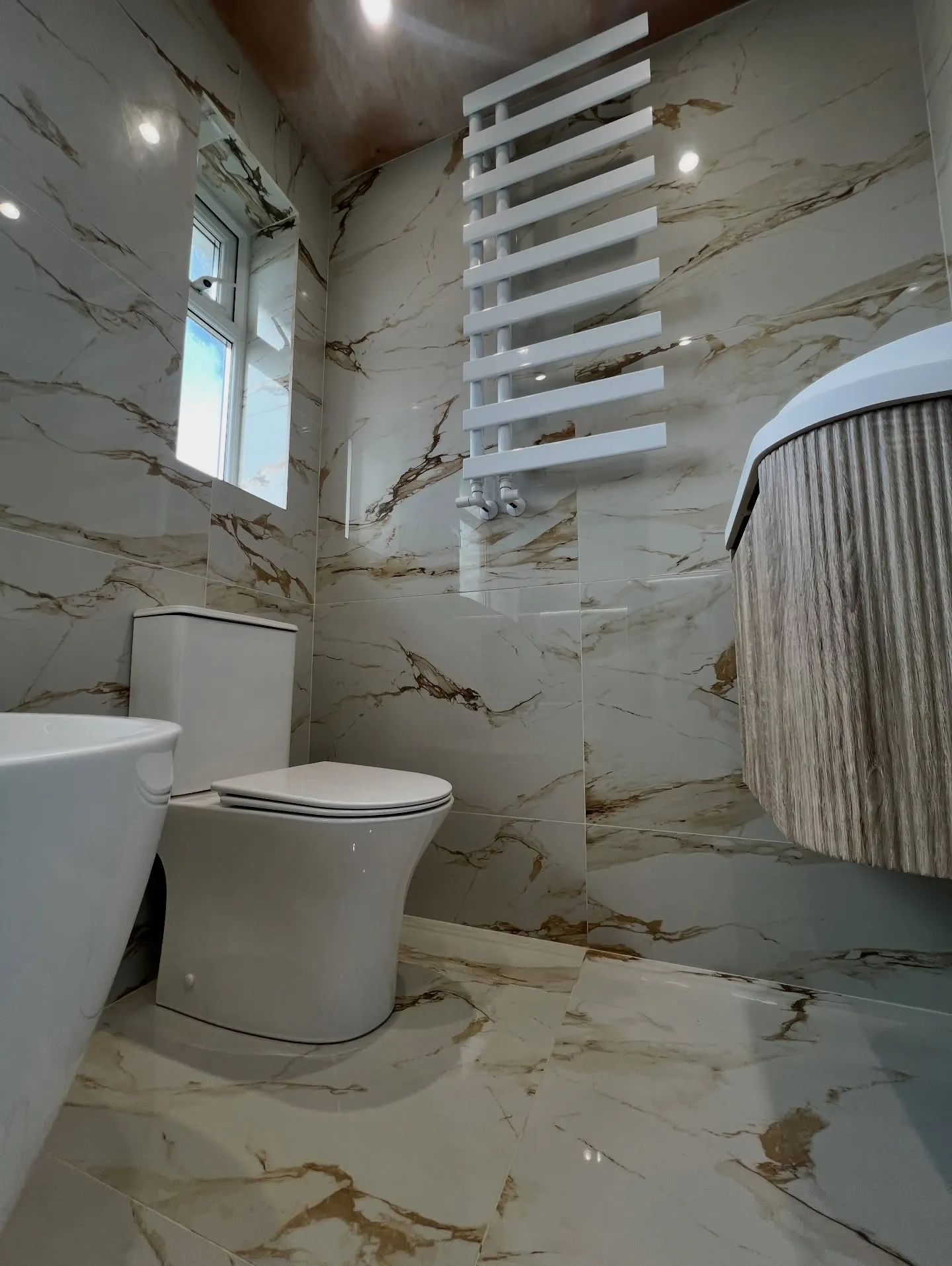 White designer towel radiator, fluted oak vanity and WC in the finished calacatta bathroom
