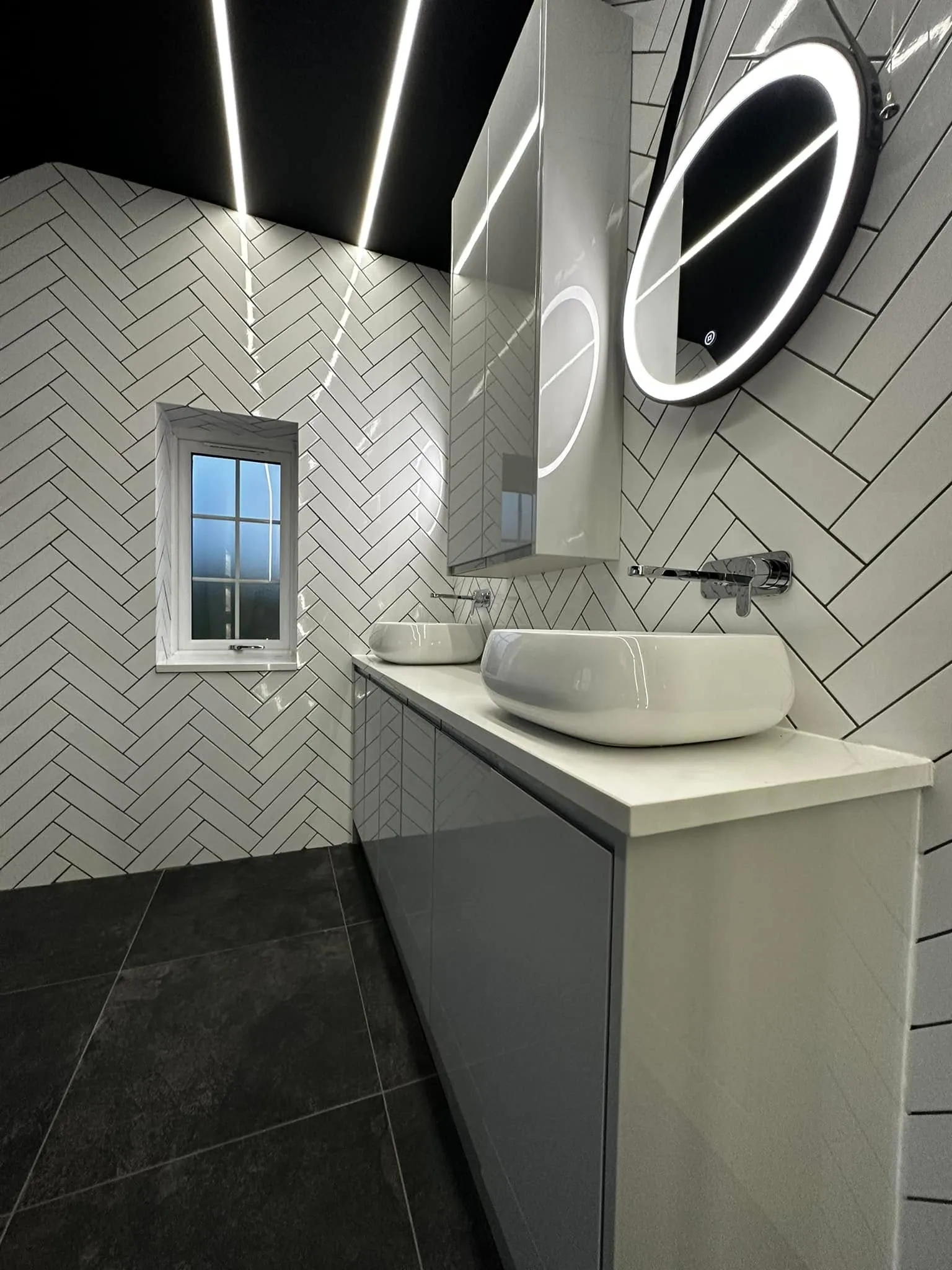 Monochrome shower room with white herringbone metro tiling, black feature ceiling with LED strip and twin countertop basins