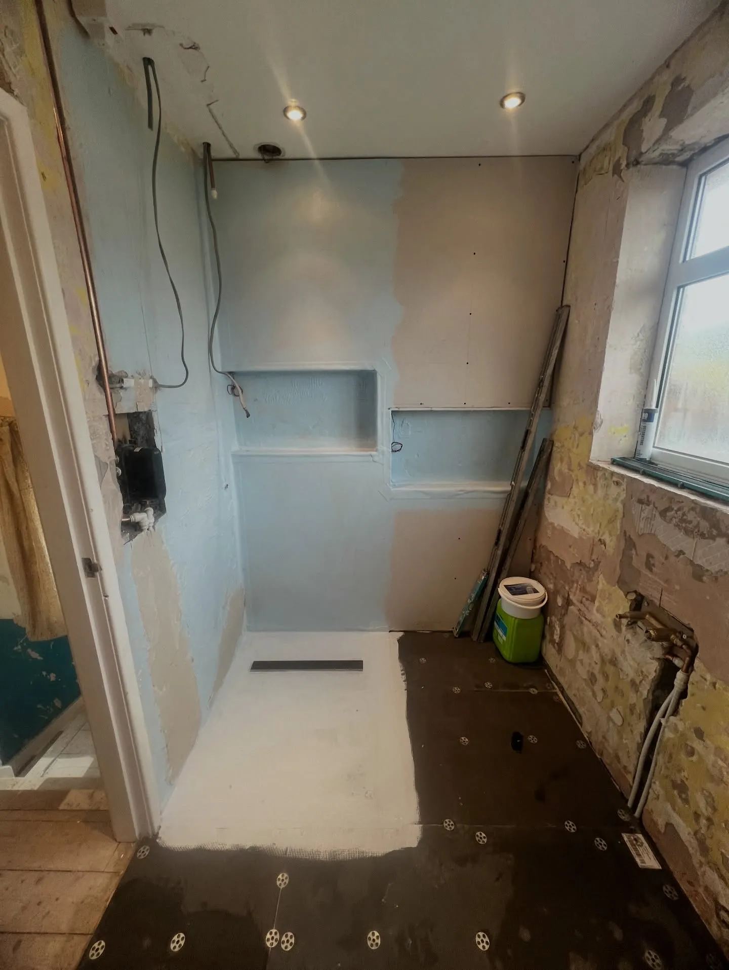 The same room mid-renovation: tanked and waterproofed shower zone with linear drain