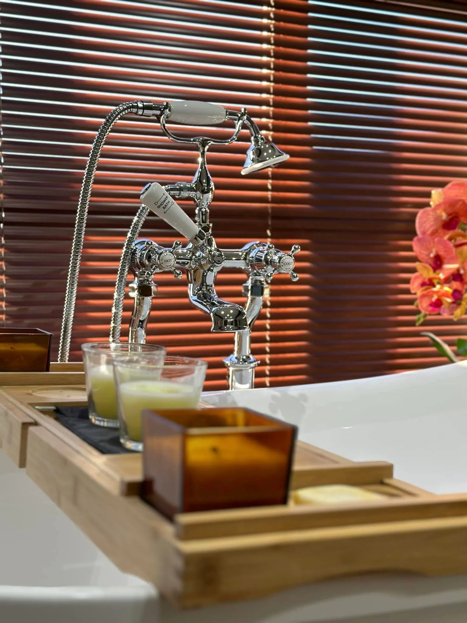 Traditional chrome crosshead bath shower mixer with white ceramic handset in warm evening light
