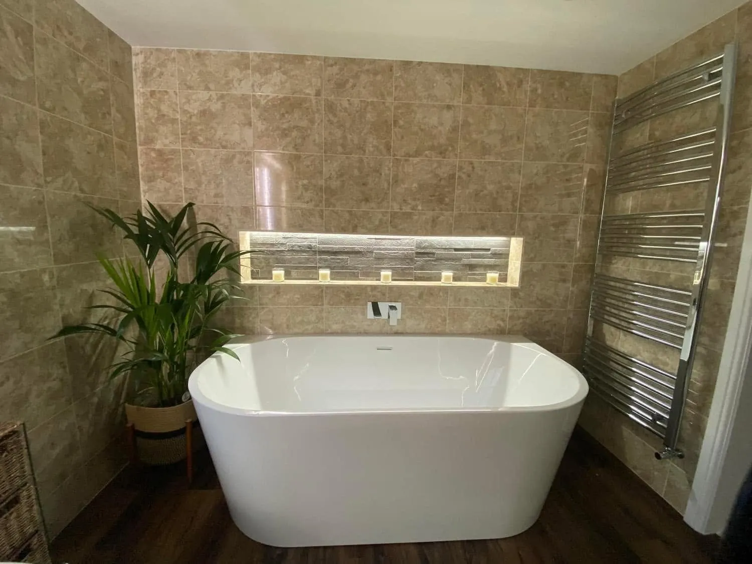 Freestanding double-ended bath beneath an LED-lit niche in split-face slate with travertine-effect walls