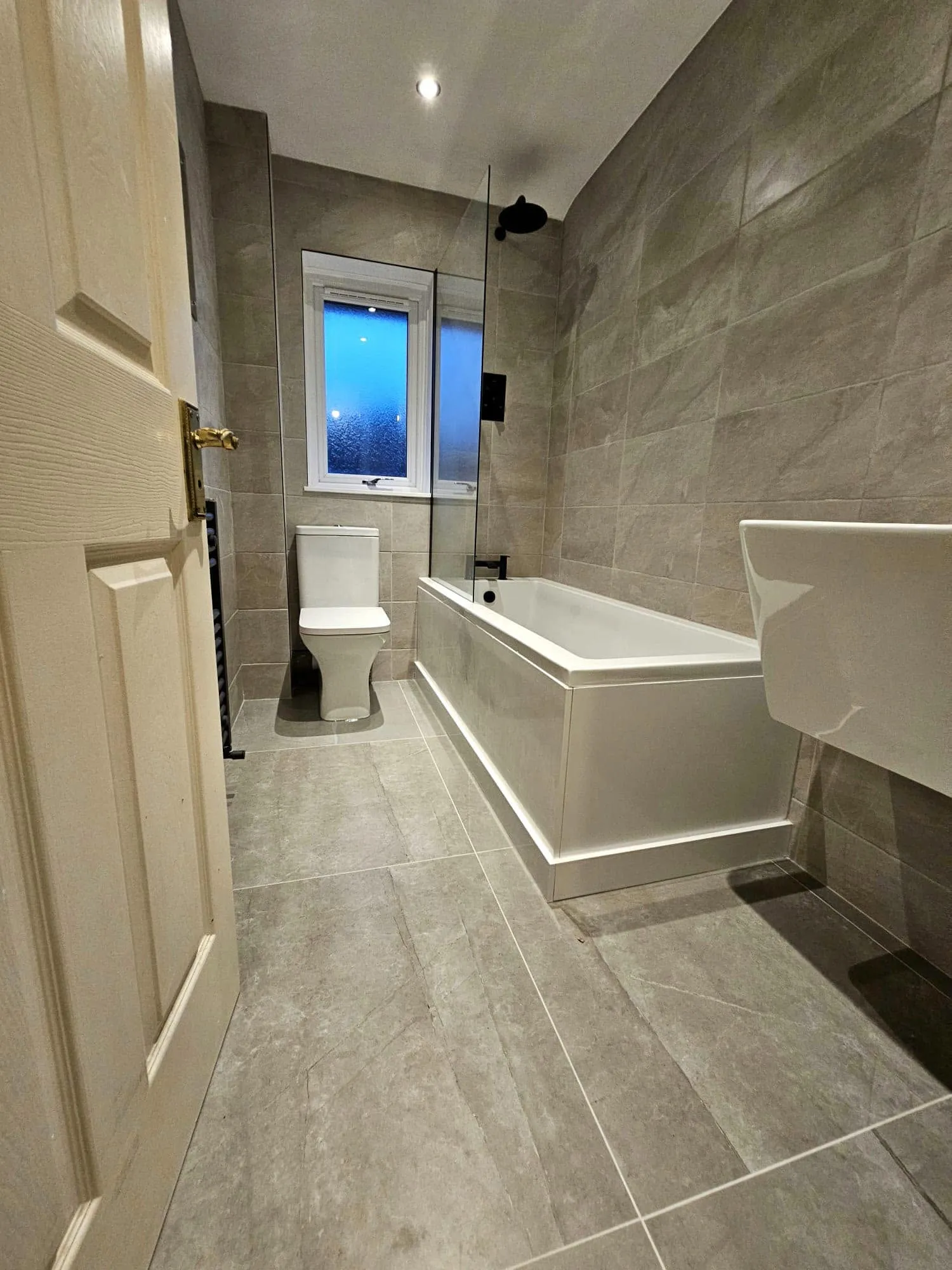 Family bathroom in large-format grey stone porcelain with hinged glass bath screen and matt black rainhead