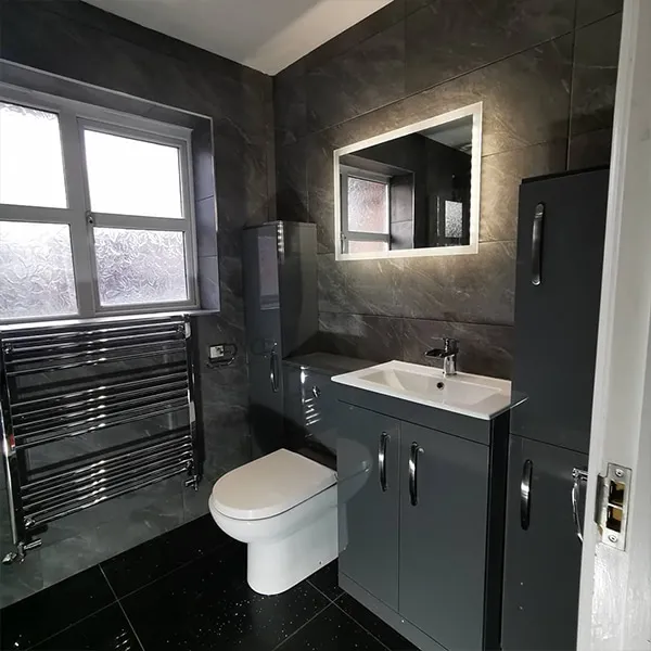 Compact bathroom in black marble-effect tiling with grey gloss vanity and illuminated mirror