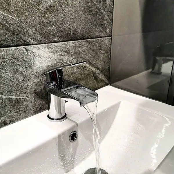 Chrome waterfall basin mixer running over a white ceramic basin against slate-effect tiling