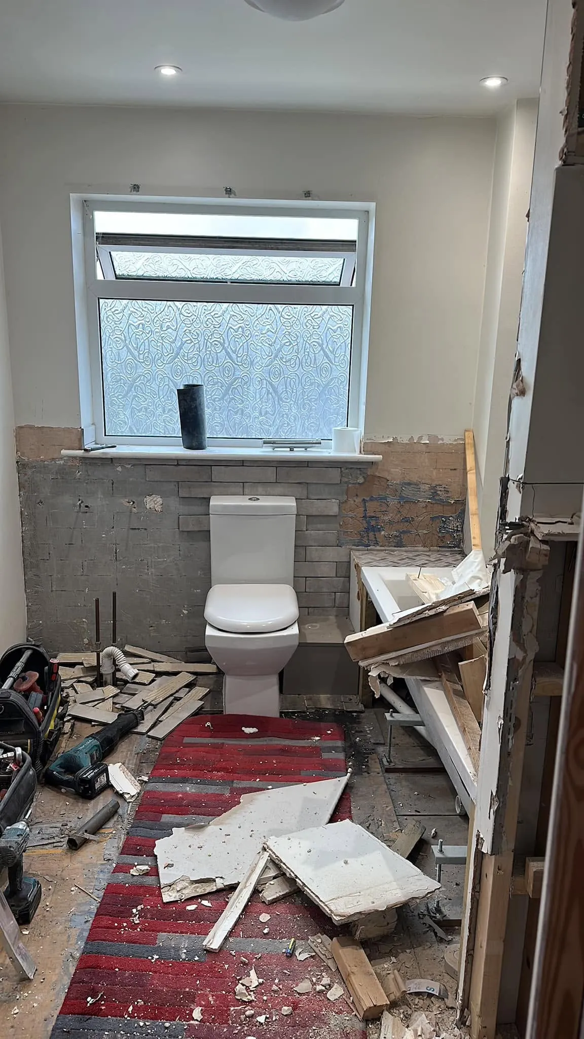 The same bathroom mid-renovation — stripped walls, exposed floor and demolition debris